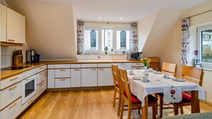 Eine Küche mit weißen Schränken, einem Esstisch gedeckt mit Tellern und Tassen, sowie einem Fenster mit Vorhängen.