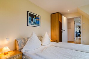 A hotel room with a bed, pillows, a nightstand, a lamp, a painting on the wall, and a wooden wardrobe.