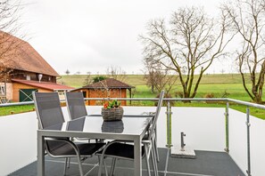 Um terraço com mesa e cadeiras, um vaso de planta e vista para uma paisagem rural.
