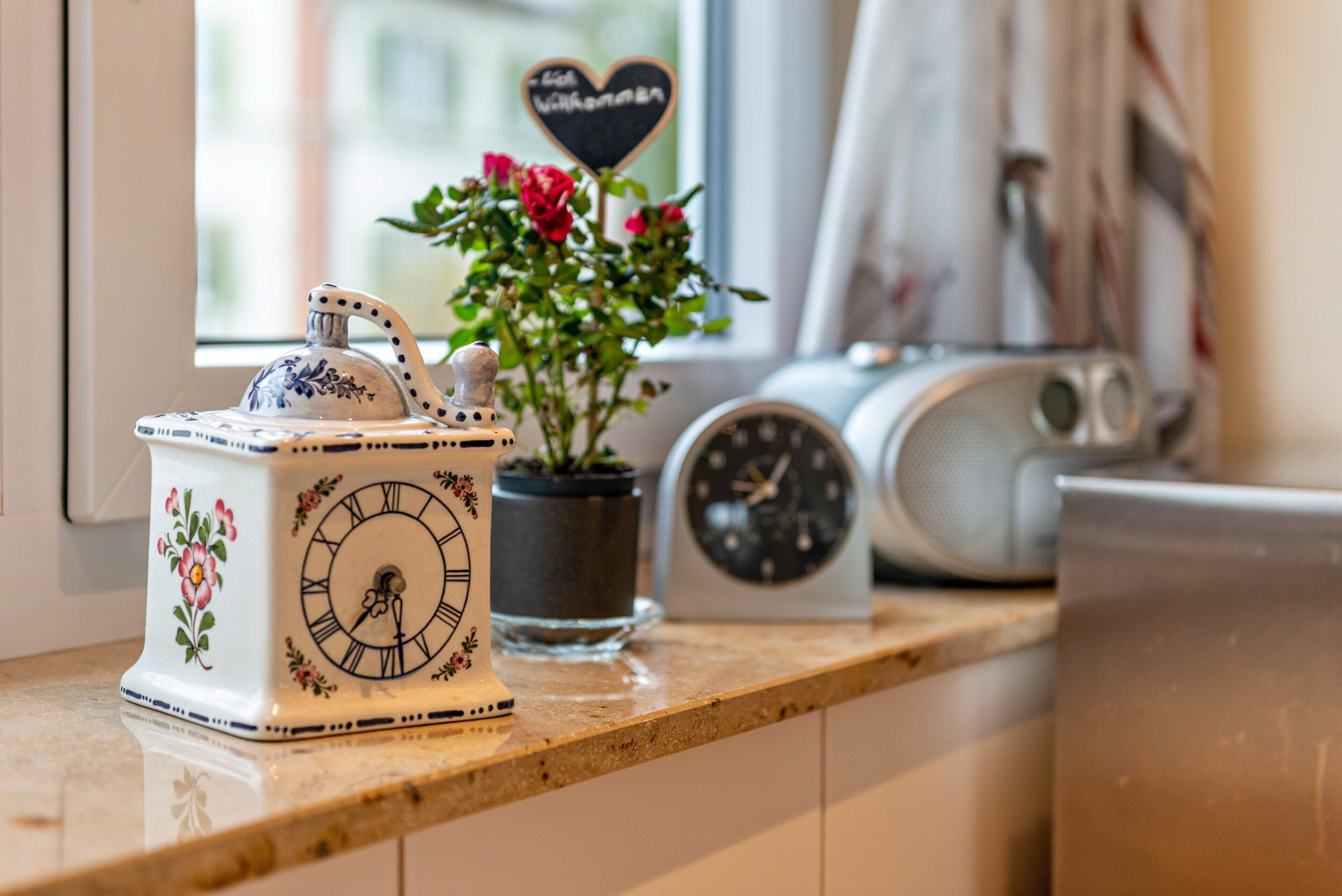 Un comptoir de cuisine agrémenté d’une horloge décorative, d’une plante en pot et d’un petit panneau en forme de cœur.
