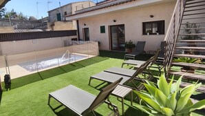 A rooftop patio with artificial grass, lounge chairs, a small pool, and a staircase.