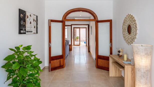A hallway with an arched doorway, a potted plant, a framed artwork, and a decorative mirror.