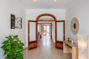 A hallway with an arched doorway, a potted plant, a framed artwork, and a decorative mirror.