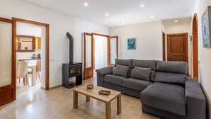 A living room with a sofa, a coffee table, a fireplace, and a kitchen area visible through an open door.