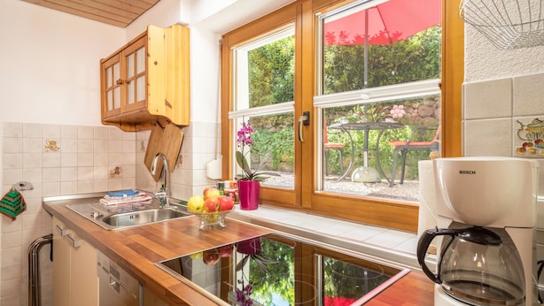 Uma cozinha com bancada de madeira, uma cafeteira Bosch, uma janela com vista para vegetação e um vaso com planta.
