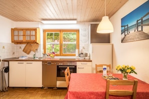 Eine Küche mit Holzausstattung, einem Fenster, einem Esstisch mit roter Tischdecke und einem Bild von einem Strand.