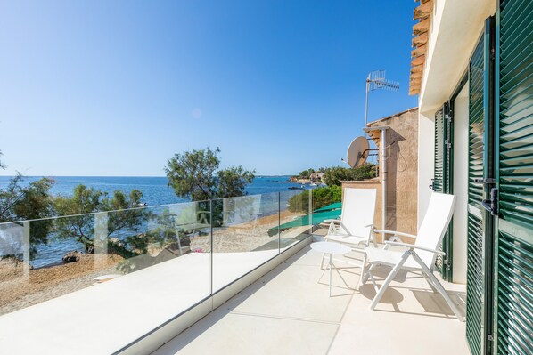 A balcony with a clear view of the sea, a pool, and a building with a satellite dish.