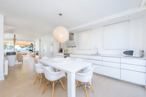 A modern kitchen with white cabinetry, a dining table with chairs, and a hanging light fixture.