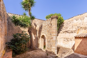 An ancient stone building with a tiled roof, a stone archway, and surrounding vegetation.