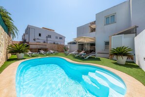 Une piscine entourée de bâtiments modernes, agrémentée de chaises longues et de plantes en pot.