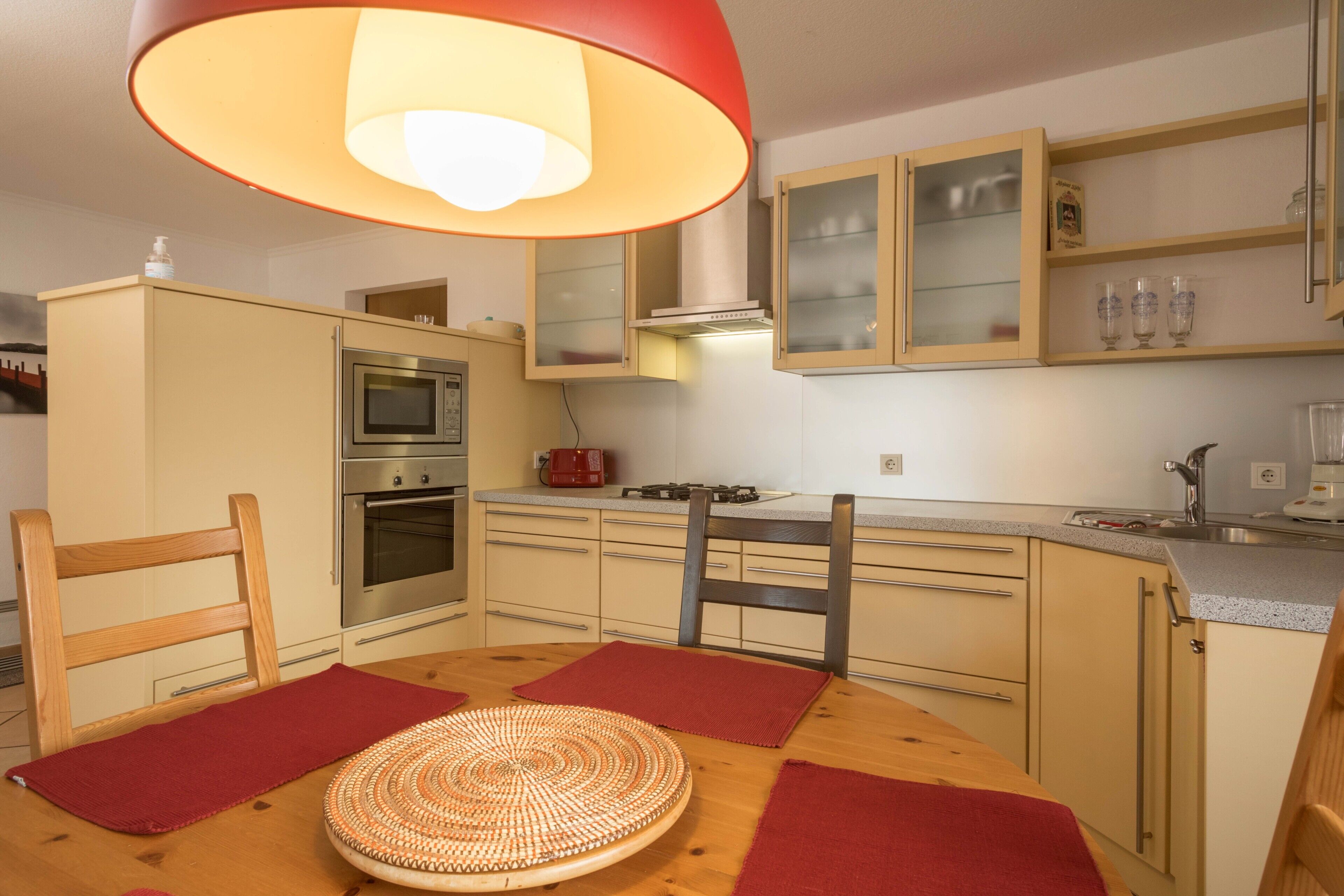 A kitchen with wooden cabinets, a stove, an oven, and a dining table with red placemats.