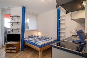 Une chambre compacte comprenant un lit, une télévision et une kitchenette.