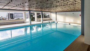 Una piscina interior amb parets de vidre transparent, un sòl de rajola i un sostre amb un dibuix de graella.