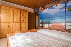 Una habitación de madera con una cama, un armario y un ventanal con vista a la playa.