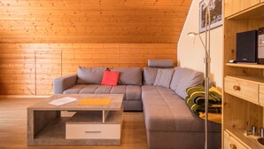 A cozy room with a wooden ceiling, a grey sofa with a red pillow, a small table with papers, and a floor lamp. - Holiday Apartment "Monika Haug" with Lake View, Mountain View, Wi-Fi, Balcony & Garden (Immenstaad am Bodensee)