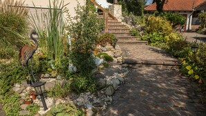 A garden pathway leading to a house with a stone staircase, surrounded by various plants and a bird sculpture. - Holiday Apartment "Monika Haug" with Lake View, Mountain View, Wi-Fi, Balcony & Garden (Immenstaad am Bodensee)