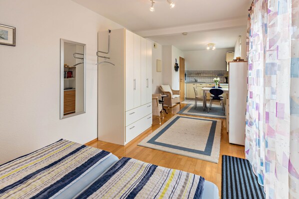 Une petite pièce comprenant un lit, une armoire, un bureau et un coin cuisine.