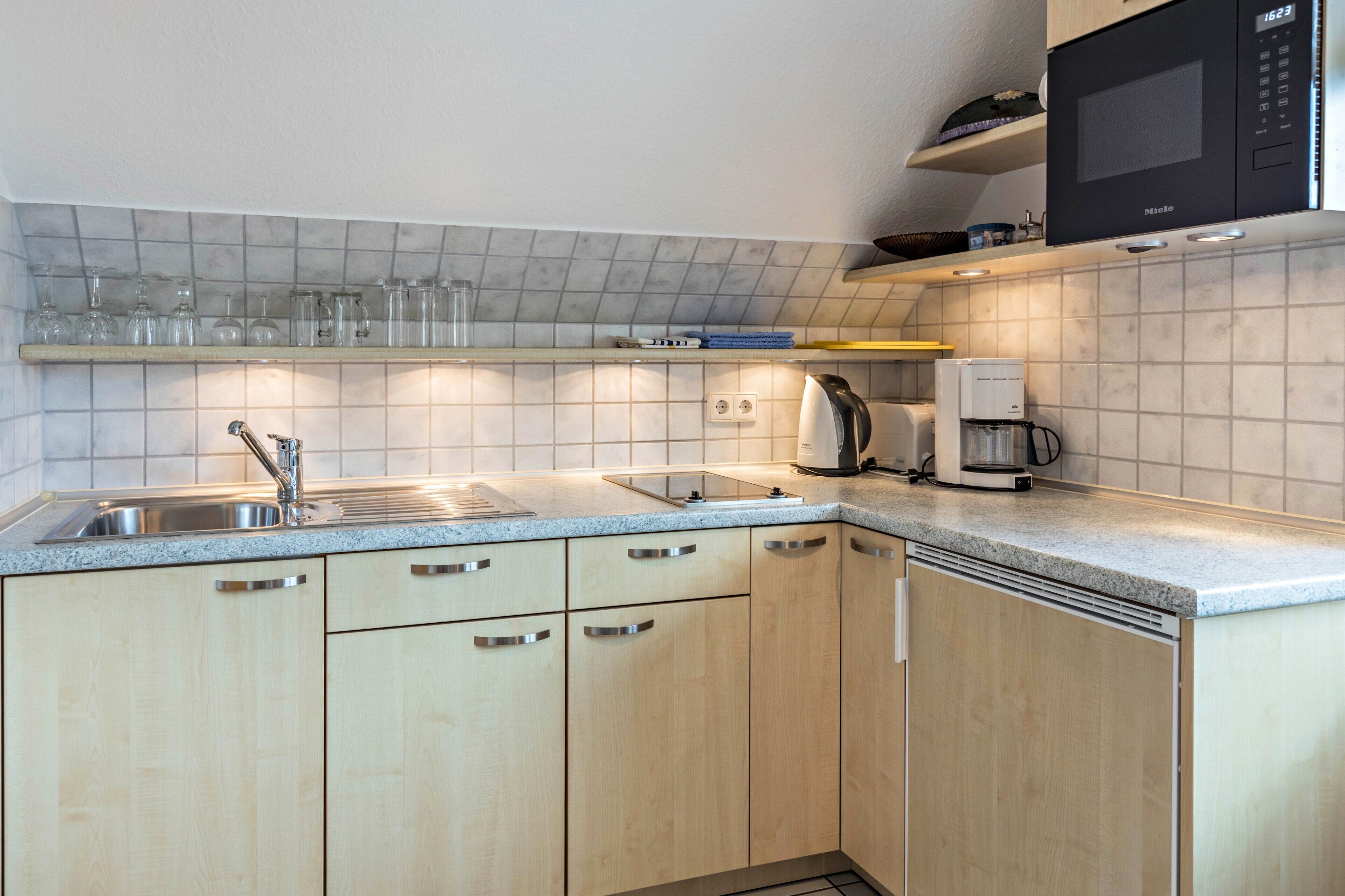 Een keuken met een spoelbak, kastjes, een magnetron en een koffiezetapparaat.