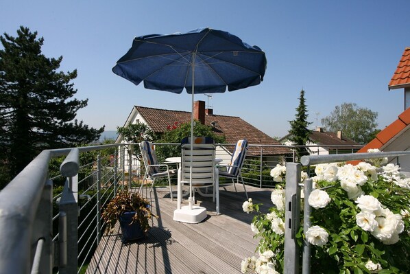 A deck with a table and chairs, an umbrella, and white flowers.