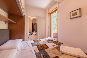 A bedroom with a bed, a window with curtains, a framed picture on the wall, and a wooden headboard.