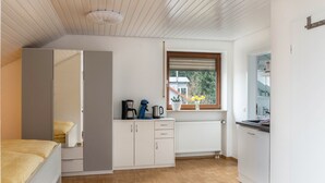 A bedroom with a bed, a wardrobe, a kitchenette with a coffee maker, and a window with a view of trees.