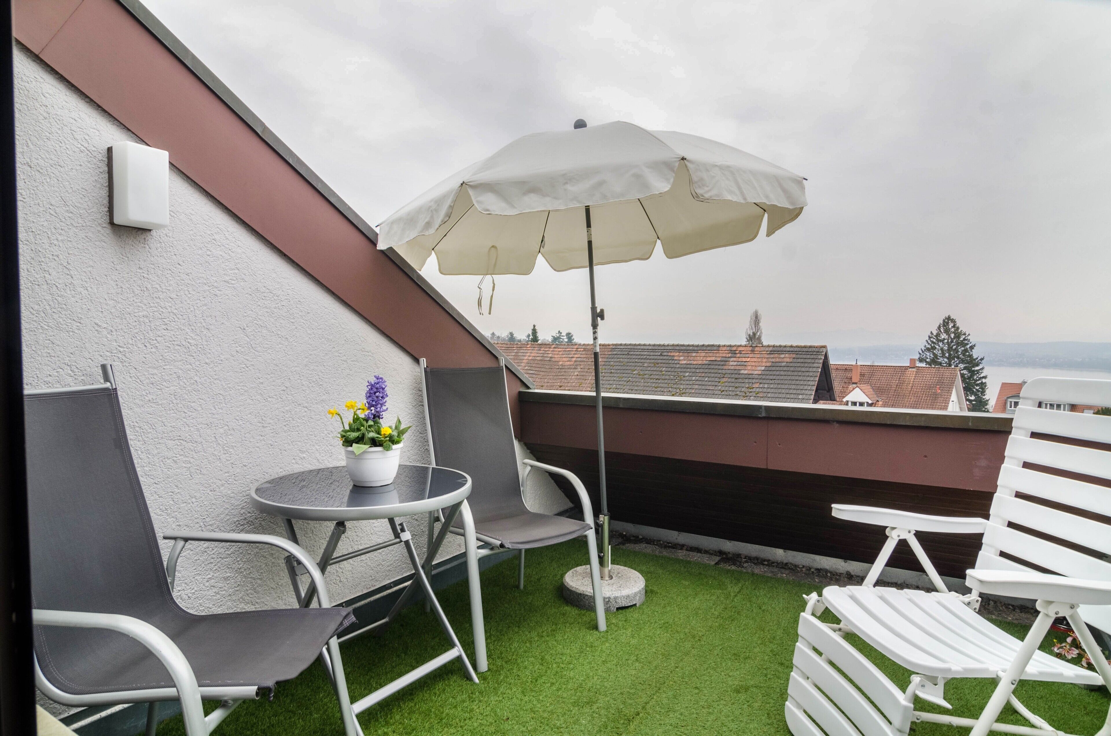 A rooftop terrace with a table, chairs, an umbrella, and a potted plant.