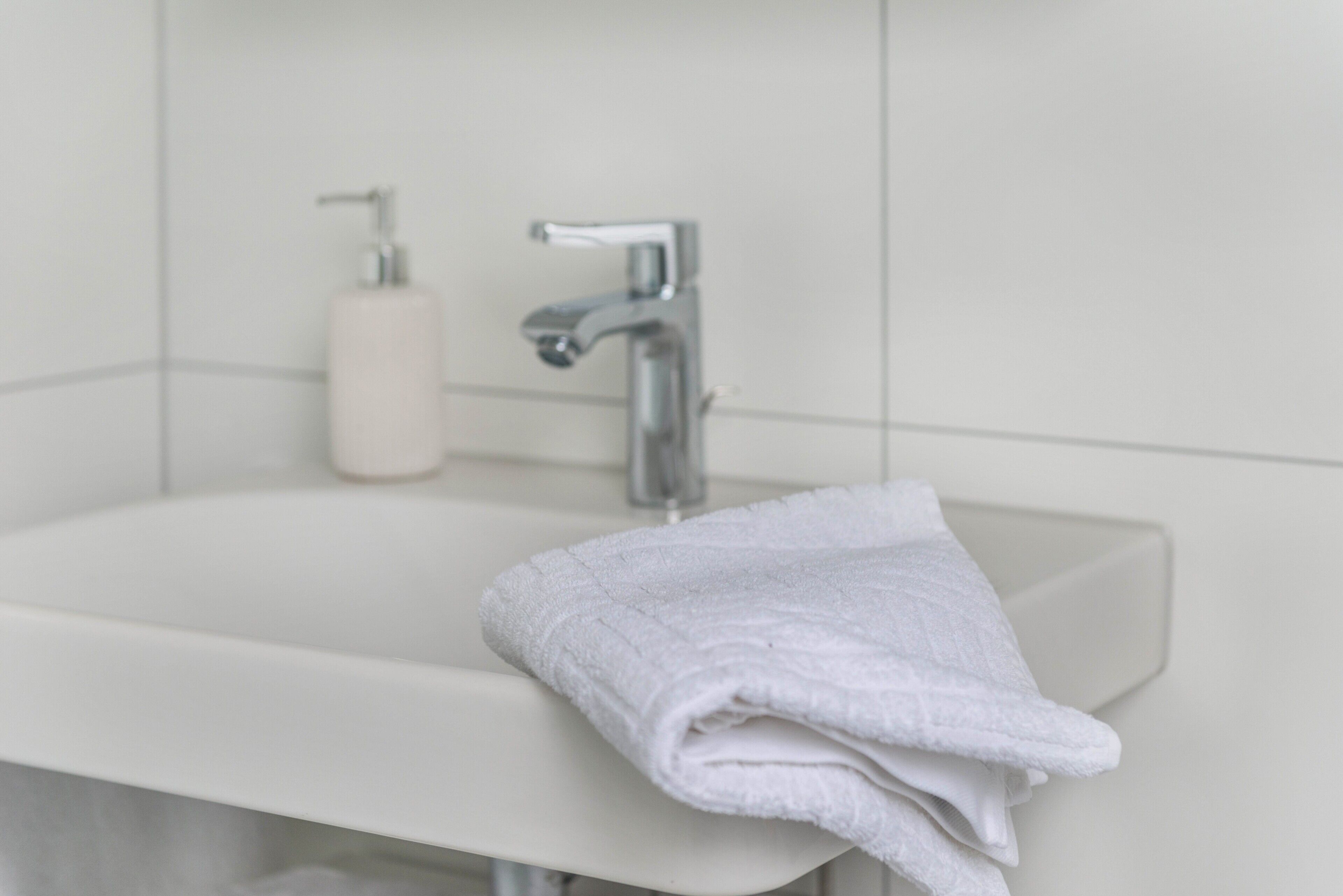 Un baño con lavamanos blanco, grifo y toalla.