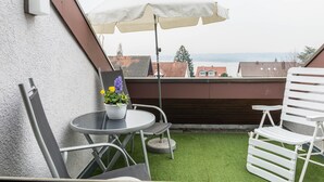 A balcony with a table, chairs, a potted plant, and an umbrella.