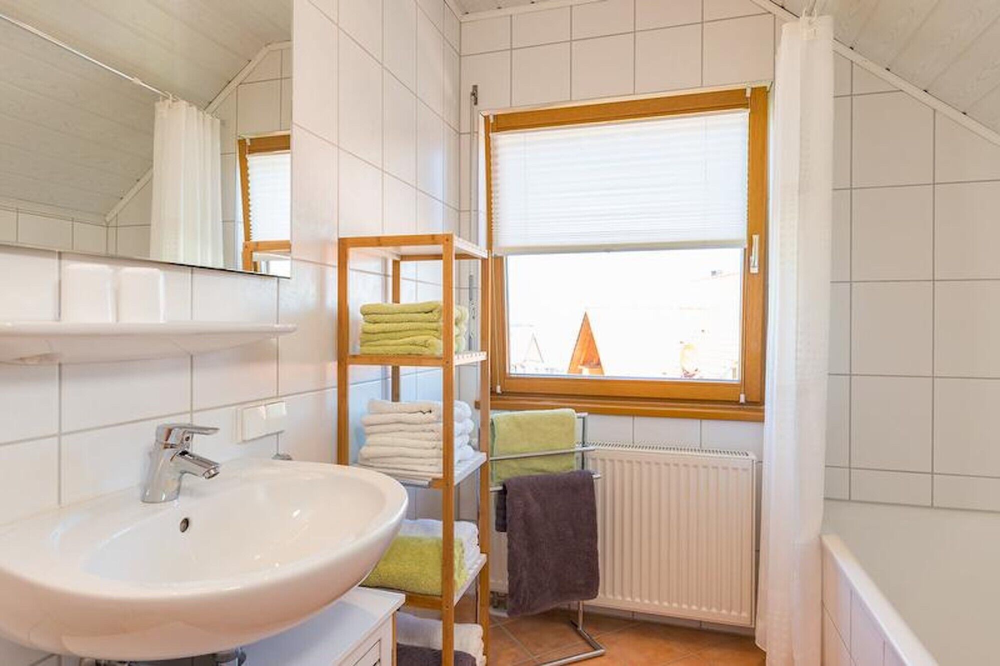 Une salle de bain avec un lavabo, des étagères avec des serviettes, une fenêtre et un radiateur.