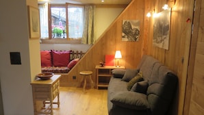 A cozy room with a wooden staircase, a sofa, a small table with a lamp, and a window with curtains.