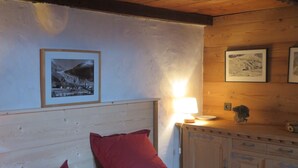 A bedroom with a wooden headboard, a bed with red pillows, a nightstand with a lamp, and framed pictures on the wall.