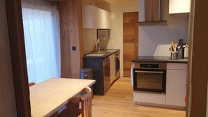 A compact kitchen with a wooden table, a sink, a stove, and a trash bin.
