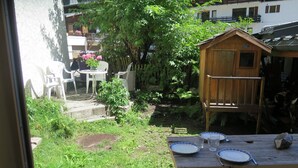 A wooden deck with a table set for two, surrounded by greenery and a wooden playhouse.