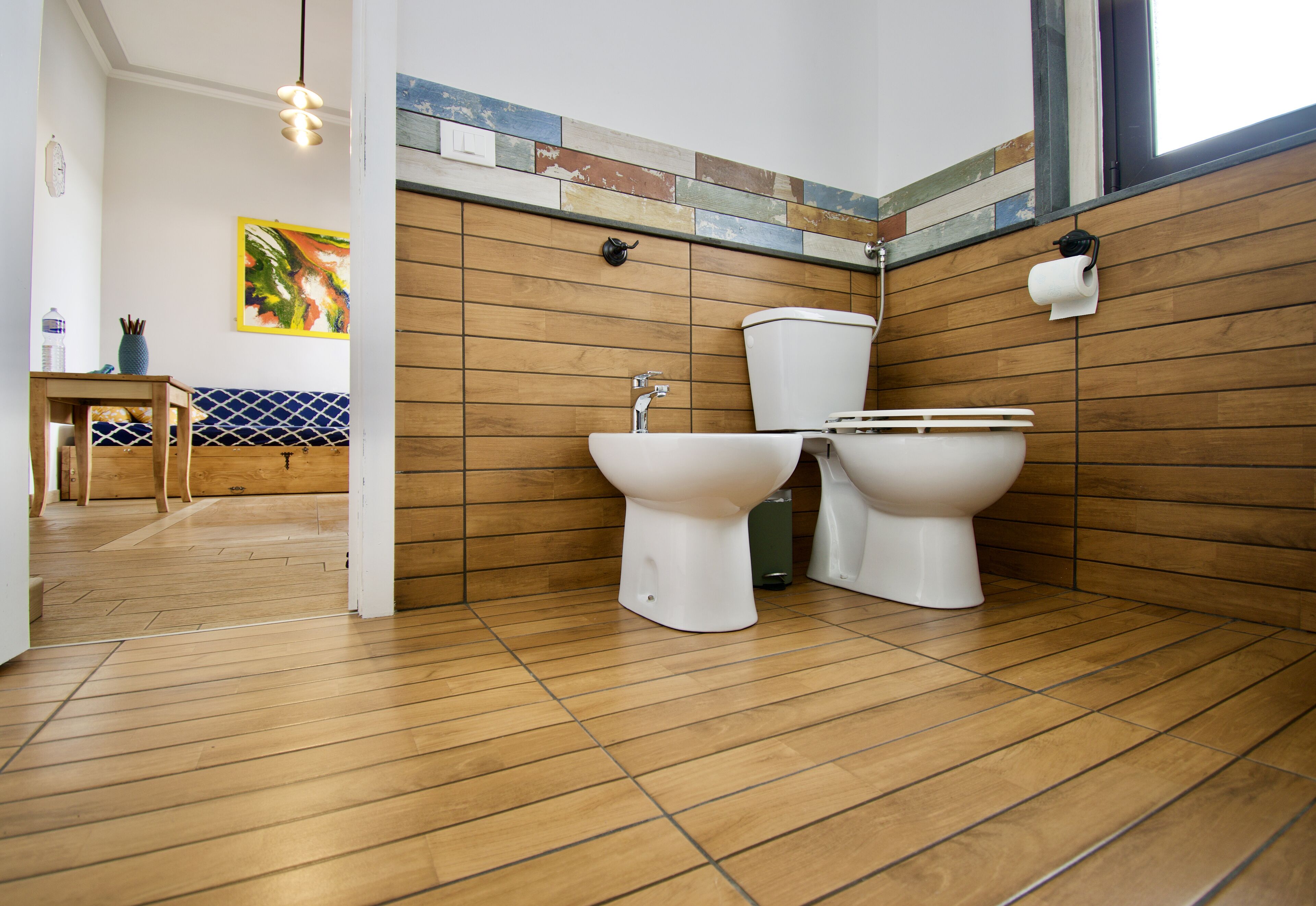 Un baño con suelo de madera, dos inodoros, un lavabo y un perchero para toallas.