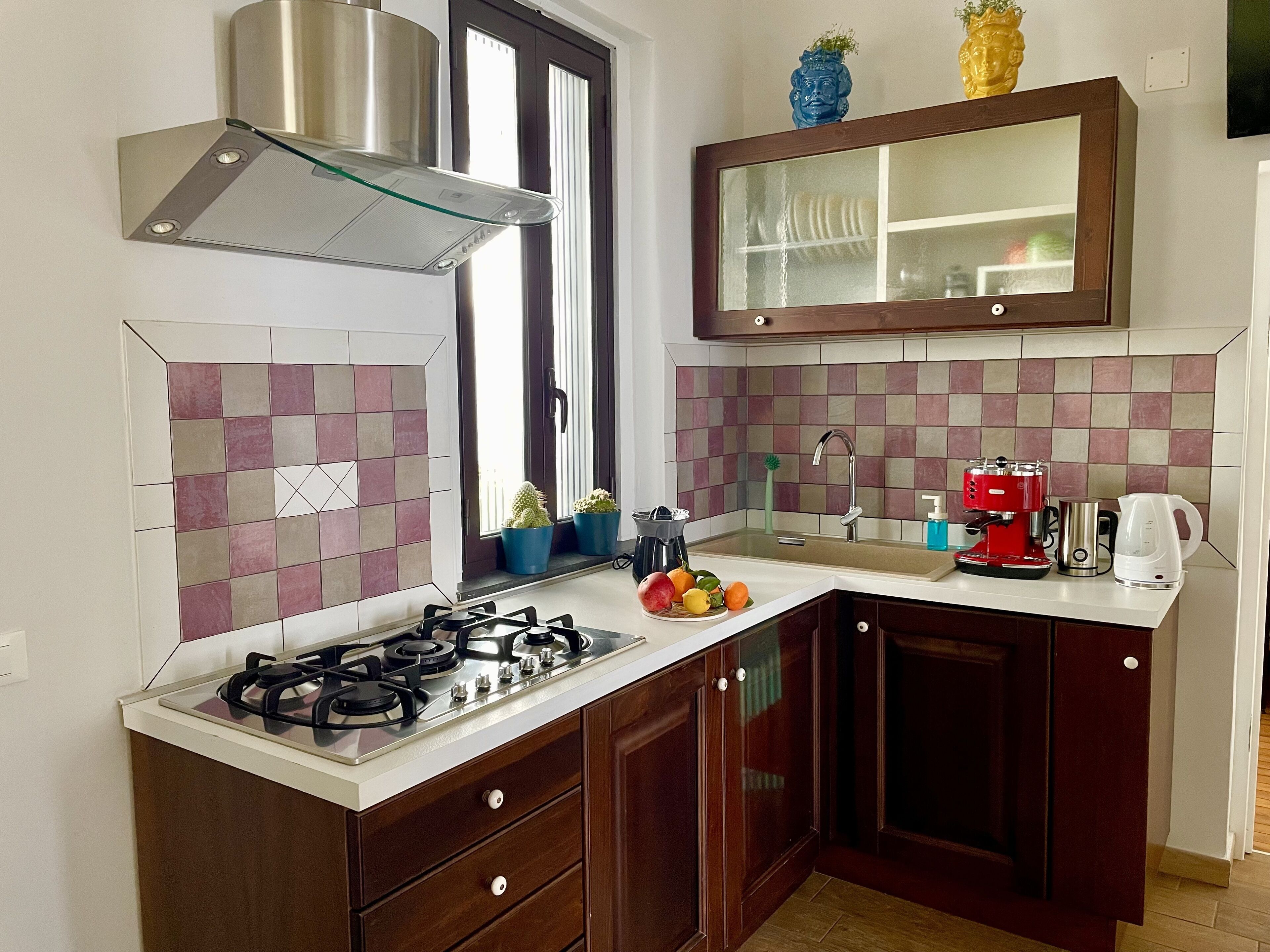 A compact kitchen with a gas stove, a stainless steel range hood, a double sink, and a wooden cabinet above the sink.
