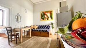 Un salon chaleureux avec un canapé en bois, une table à manger avec des chaises, un petit coin cuisine et une grande fenêtre.