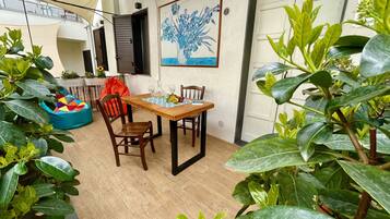 Zona pranzo con tavolo e sedie in legno, un pouf colorato e un quadro con fiori al muro.