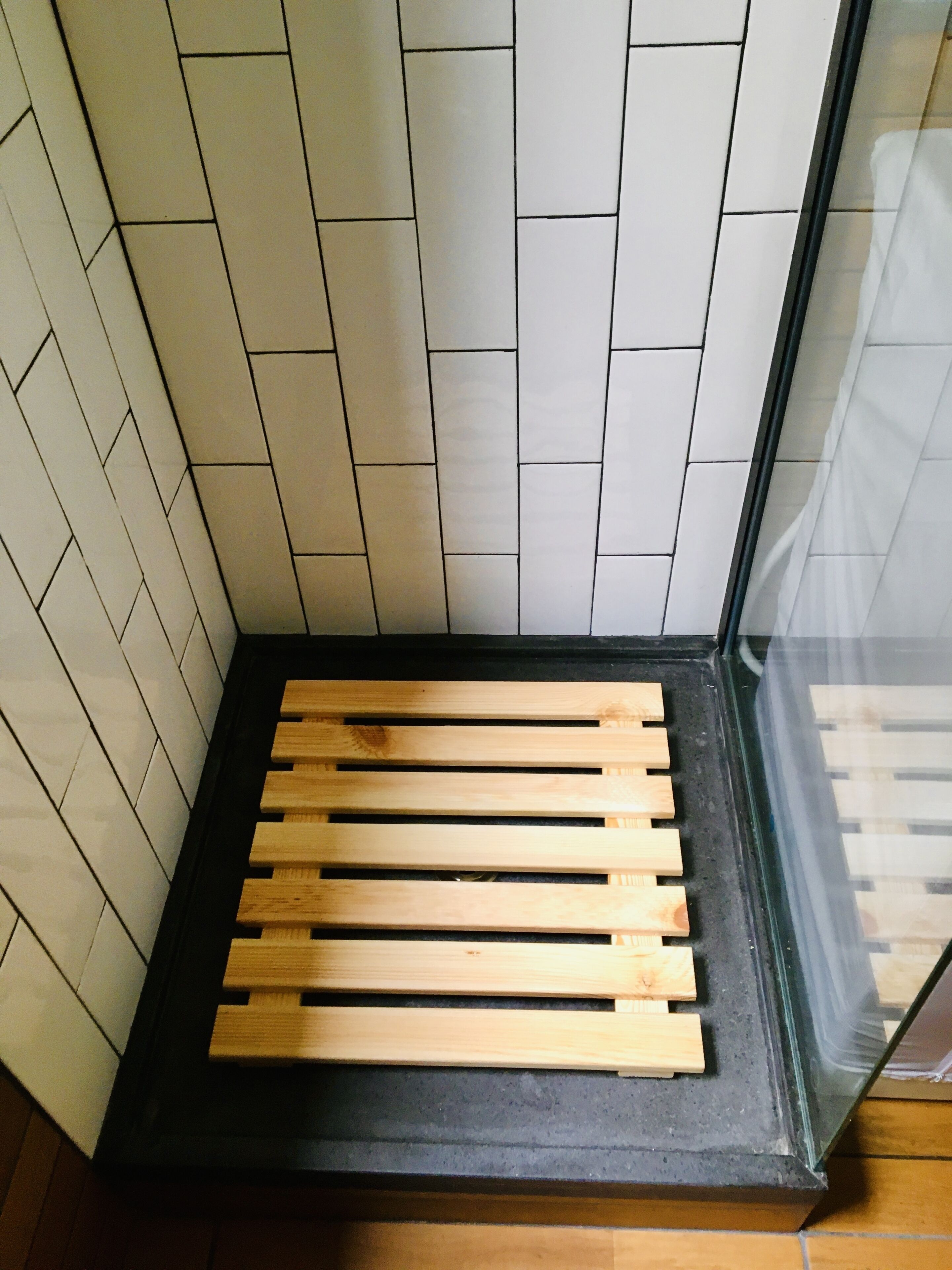 A corner of a room with a wooden bench, white tiled walls, and a glass door.