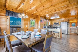 A wooden cabin interior with a dining area, kitchen, and a view of the outdoors.