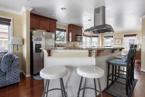 Una cocina con armarios de madera, un refrigerador de acero inoxidable, un microondas y una isla grande con taburetes.
