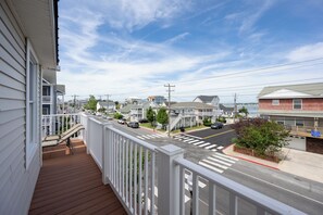 Una calle residencial con casas, cielo despejado y una terraza de madera con barandilla.