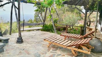 Un patio de piedra con sillones de madera y un columpio.