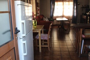 Een keuken met een koelkast, een eettafel, stoelen en een raam met gordijnen.