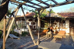 A rustic outdoor seating area with wooden benches and a swing set, surrounded by stone flooring and a thatched-roof structure. - Traditional Canarian Retreat: Casa Francisco with Private Pool, Terrac (Puntagorda)