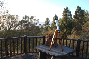 A telescope on a stone platform with a railing, surrounded by trees and a clear sky.