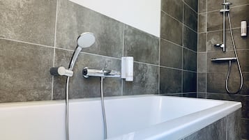 A modern bathroom with a freestanding bathtub, a handheld showerhead, and a wall-mounted faucet.