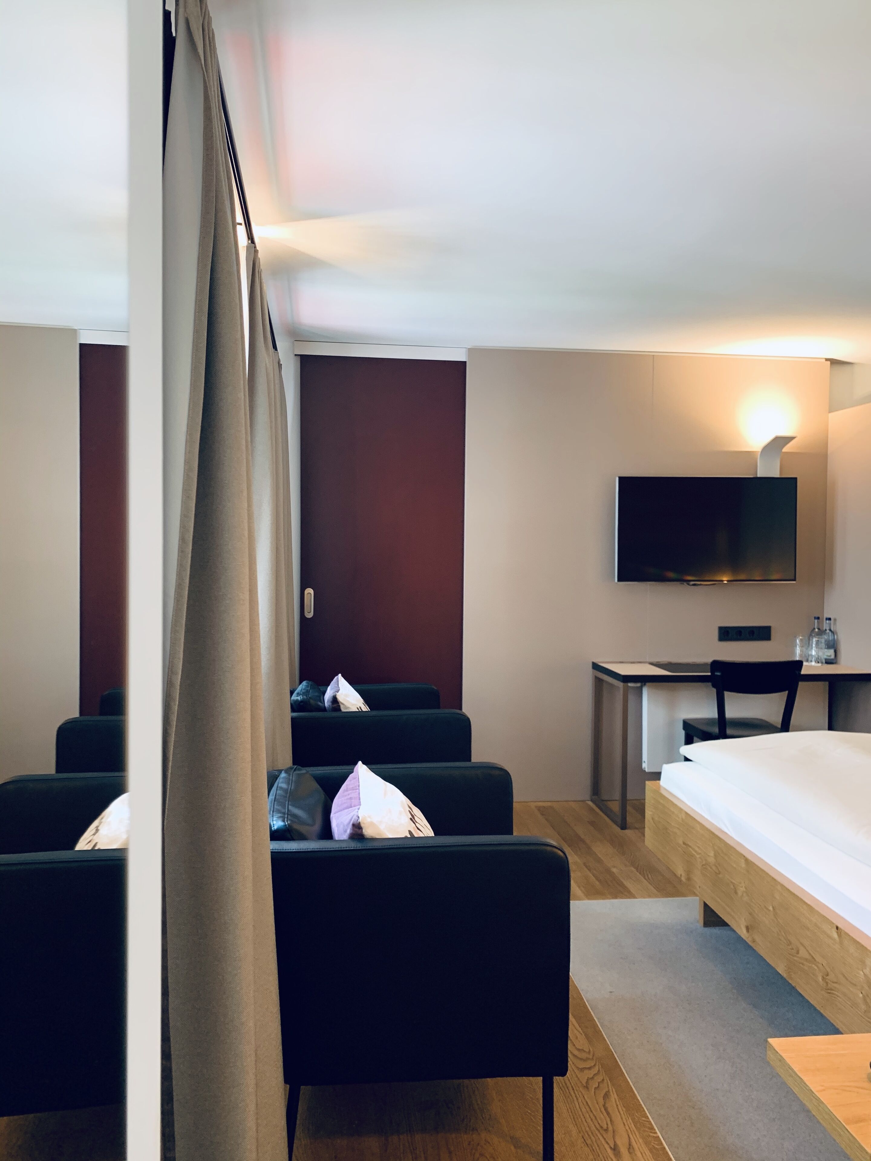 A hotel room with a bed, a desk, a television, and two sofas.