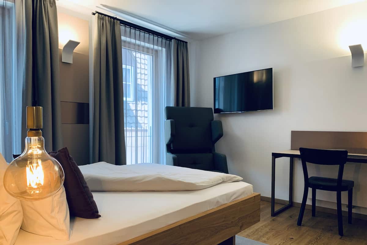 Une chambre d’hôtel moderne avec un lit en bois, un bureau, une chaise, une télévision et une lampe.