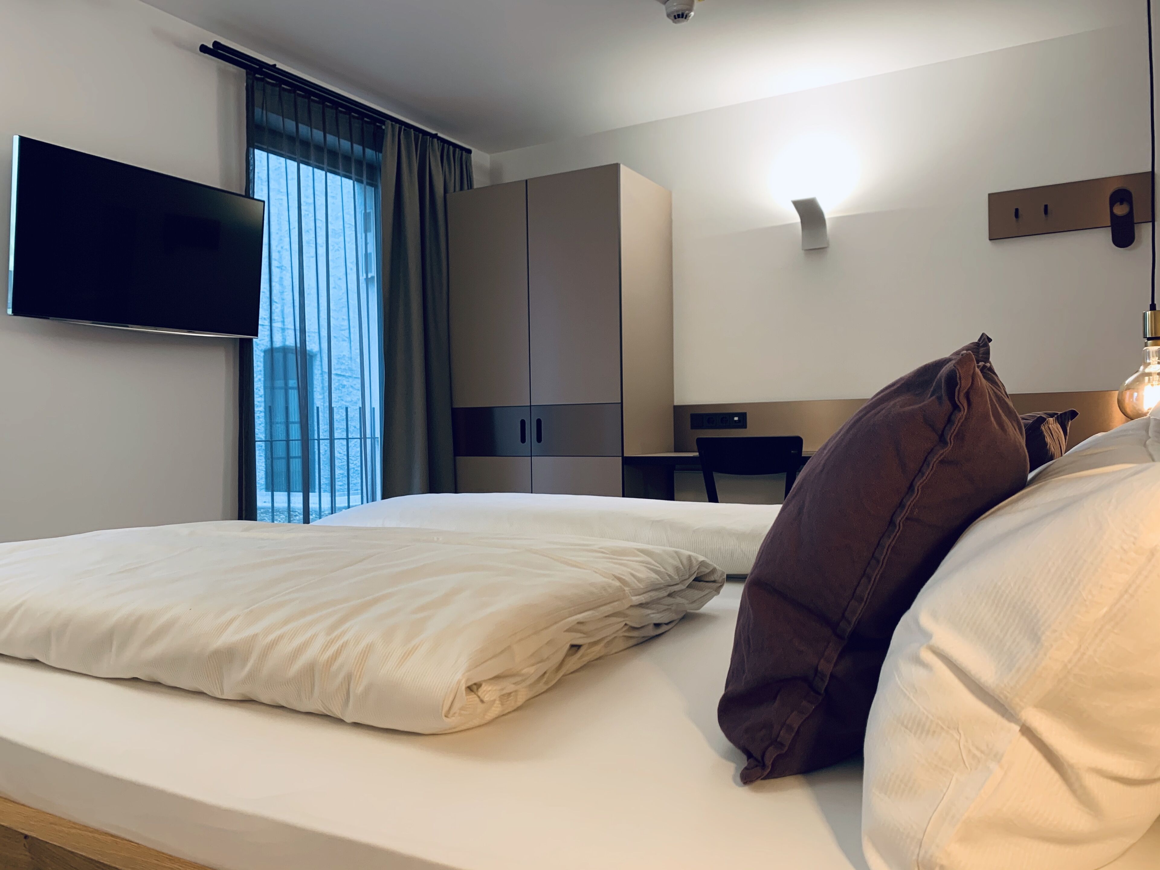 Una camera d'albergo con un letto, una scrivania, una sedia, una televisione e un armadio.