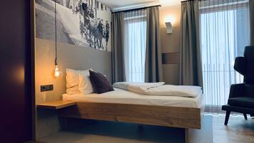 Une chambre d’hôtel moderne avec un grand lit, une tête de lit en bois, une lampe fixée au mur et une grande fenêtre avec des rideaux.